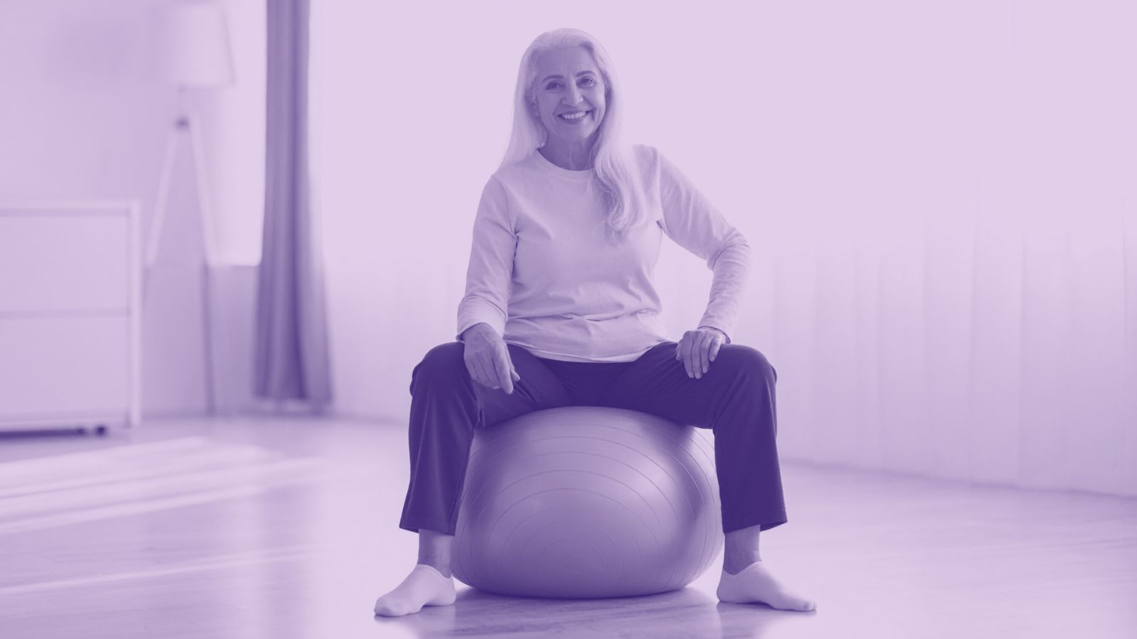Senior woman sitting on exercise ball in fitness studio