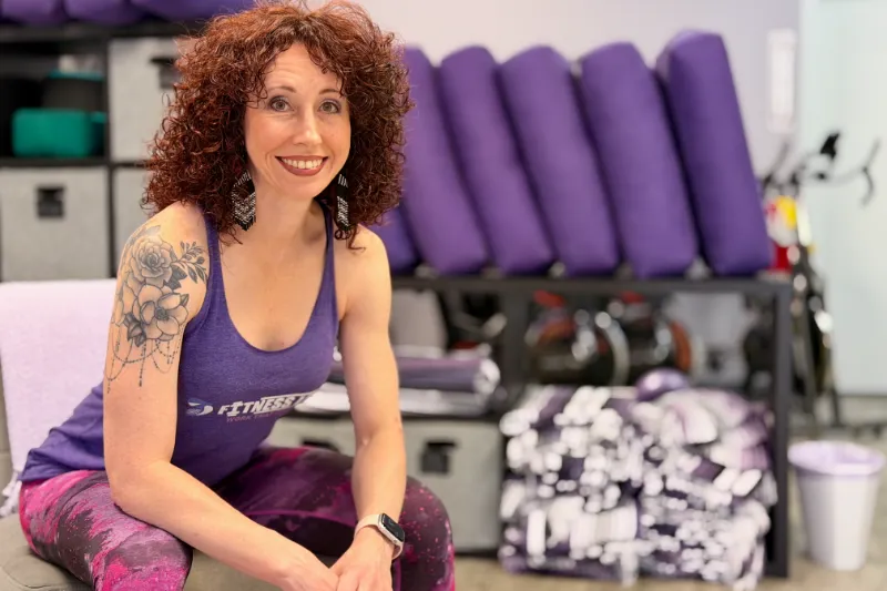 Stephanie Gilbert - Group Fitness Instructor Stephanie Gilbert, a smiling fitness instructor seated in a studio